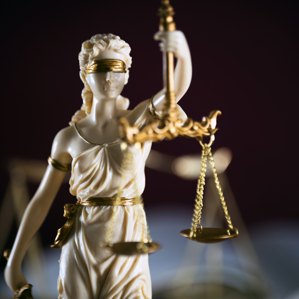 AbraCasaBra.se Närbild av en staty av Justitia med ögonbindel som håller i en balanserad våg, en symbol för rättvisa och lag, mot en mörk bakgrund.